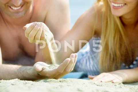 Close-up of smiling couple lying on the beach and playing with sand Stock Photos