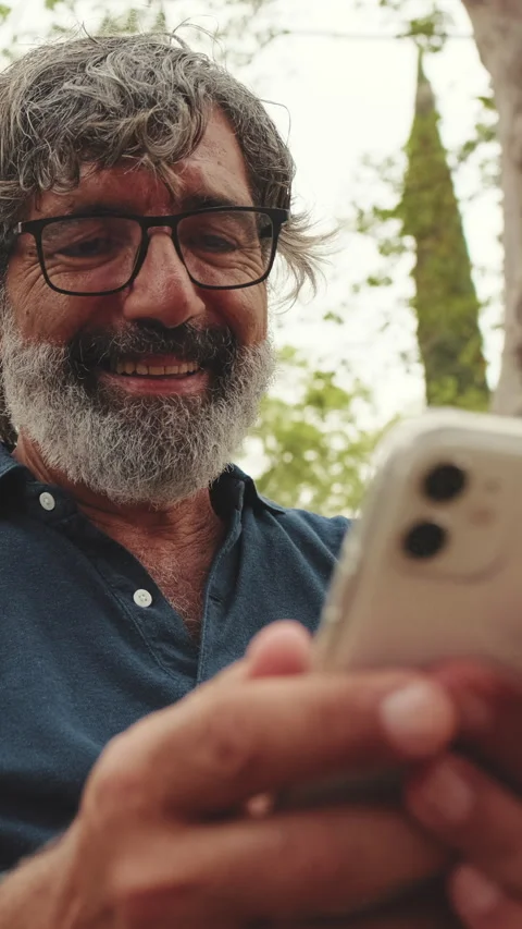 Close-up of smiling elderly man using phone while sitting in park Stock Footage 252503933