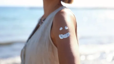Close up of a smiling face drawn with sun cream on a girl's arm by the ocean Stock Footage 279263258