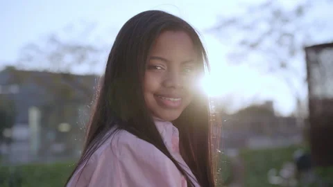Close-up of a smiling girl looking at the camera with the sun against the lig Stock Footage 153250879