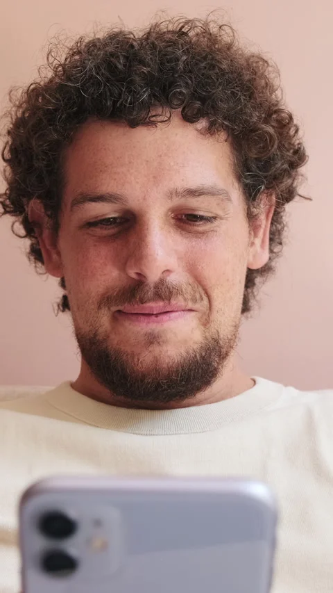 Close up, smiling guy sitting on the sofa in cozy living room scrolls across the Stock Footage 250840520