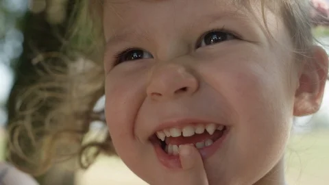 CLOSE UP: Smiling little curly haired girl looks around the sunny tree avenue. Stock Footage 89949694