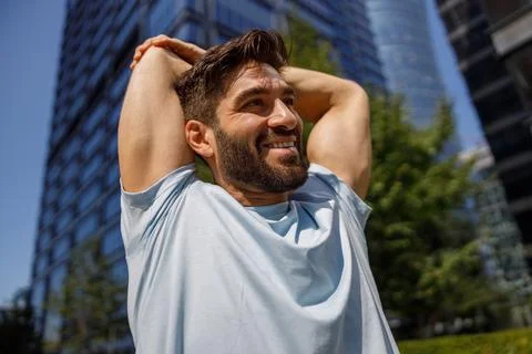Close up of smiling man doing stretch on modern city skyscrapers background Stock Photos