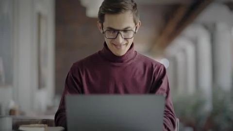 Close-up of smiling man in stylish glasses and turtleneck working at laptop in 스톡 동영상 343513985