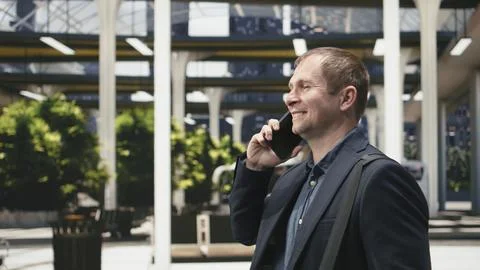 Close up of smiling man walking through bus station while speaking on phone Photos