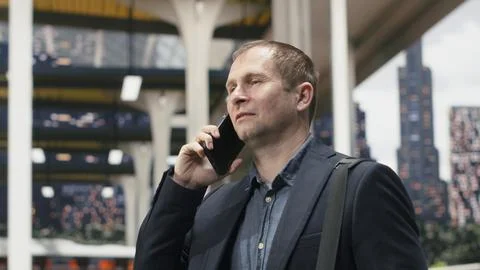 Close up of smiling man walking through bus station while speaking on phone Photos
