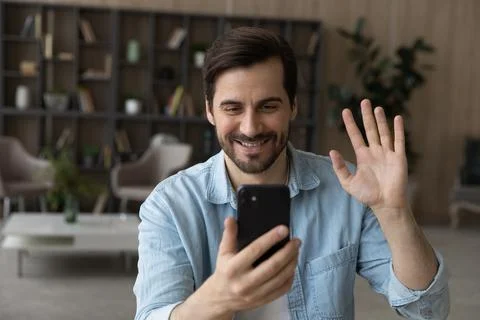 Close up smiling man waving hand at smartphone webcam, chatting Stock Photos