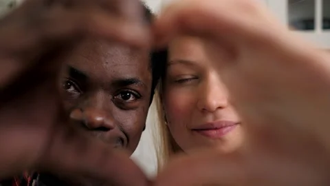 Close up smiling multiethnic couple faces looking through joined fingers heart Stock Footage 190496579