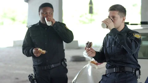 Close up smiling two policemen drinking coffee and eating donut with appetite Stock Footage 112956866