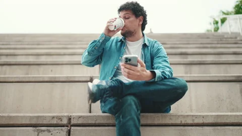 Close-up of smiling young bearded man in denim shirt sitting on high steps and Video stock 226980909