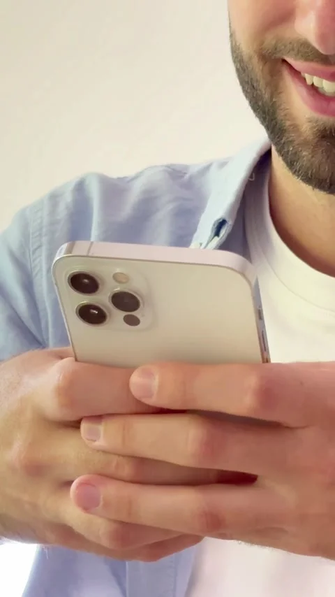 Close-up of a smiling young man with a beard holding a modern smartphone Vídeos de archivo 344781494