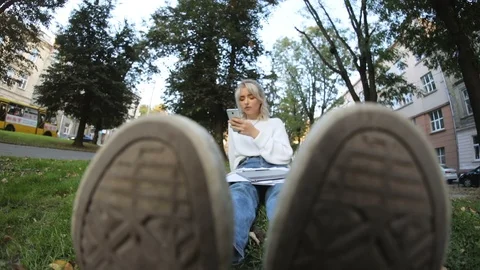 Close-up of sneaker. Portrait of likable young girl student sitting on grass Stock Footage 100570485