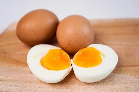 A close-up soft-boiled egg cut into two halves in the foreground with two w.. Stock Photos