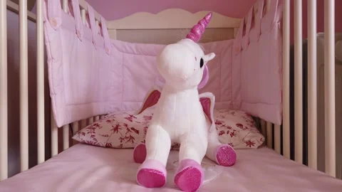 Close up of a soft unicorn toy at white children bed. baby cot Stock Footage 148411040