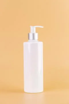 Close-up on a soft yellow background white glossy bottle with dispenser Stock Photos