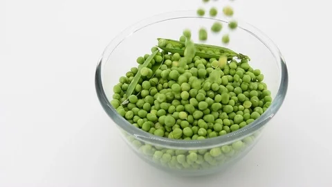 Close up of some peas falling from the top into a glass bowl. White background. 库存影片 108211130