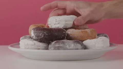 Close up of Someone Sneaking a Donut From a Plate in Front of a Red Backdrop Stock Footage 208762486