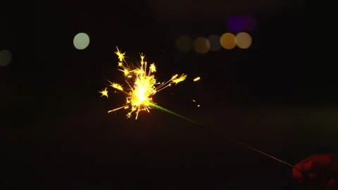 Close on sparkler burning in slow motion with fireworks launching in background Stock Footage 248085894