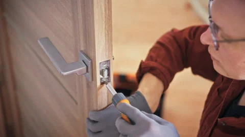 A close-up of a specialist in gloves working on a door handle lock with an o Vidéo 341490956