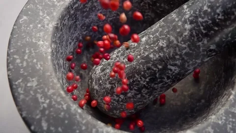 Close-up of spicy rose peppercorns falling into the grey stone mortar Stock Footage 294419780