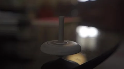 Close up of spinning top on glass table wobbling and falling down Stock Footage 257777546