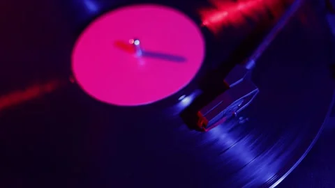 Close-up of a spinning vinyl record with vibrant pink label and blue lighting Stock Footage 339003585