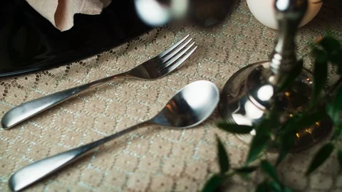 Close-up of a spoon and fork lying on a tablecloth to the right of a black plate Stock Footage 97719880