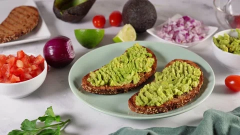 Close up of a spoon placing small pieces of tomato on the top of avocado toasts Stock Footage 136872009