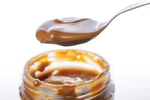 Close up of spoon scooping dulce de leche out of a jar, traditional sweet f.. Stockfoto's