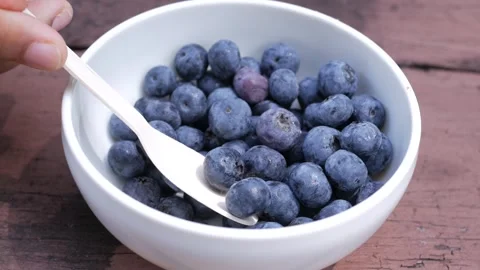 Close up of spoon scooping fresh blueberries from white bowl outdoors. 스톡 동영상 333156074