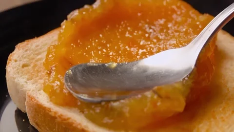Close up of spoon spreading orange marmalade on toast bread Stock Footage 289411835