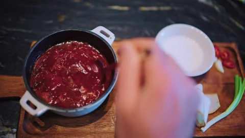 Close up of a spoon stirring borscht inside a small pot placed on a wooden board Stock Footage 329393416