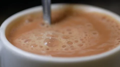 Close up of spoon stirring frothy tea in white mug dynamic motion. Stock Footage 332192682