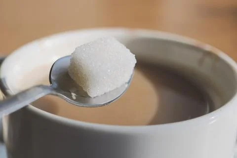 Close up of spoon with sugar cube above cup of coffee in a kitchen Stock Photos