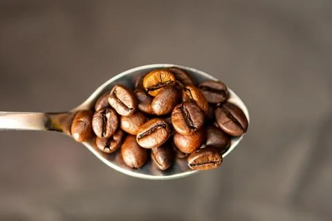 Close up spoonful of roasted coffee beans on blurred background Foto stock