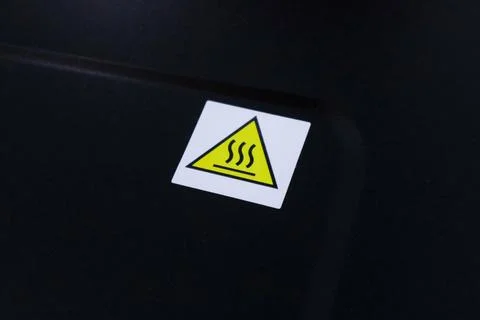 Close up of a square sticker with a yellow triangular hot surface warning s.. Stock Photos