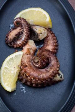 Close up squid tentacles with lemon on black plate Stock Photos