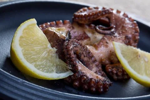 Close up squid tentacles with lemon on black plate Stock Photos