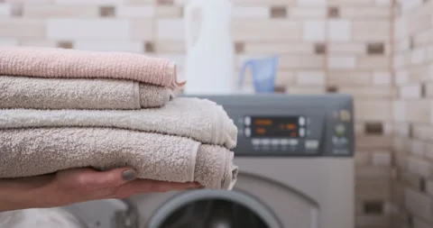 Close-up stack of clean towels in female hands on washing machine Stock Footage 230094106