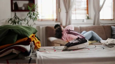 Close up of stack of clothes and hot iron left on ironing board Stock Footage 229245679