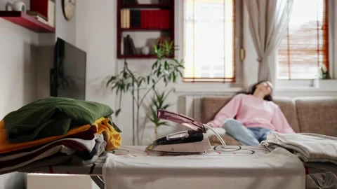 Close up of stack of clothes and steaming hot iron left on ironing board. Stock Footage 231294839