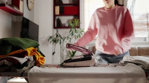 Close up of stack of clothes and steaming hot iron left on ironing board. Stock Footage 234704589