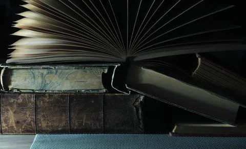 Close up of a stack of old books, one opened on dark background, education Stock Photos