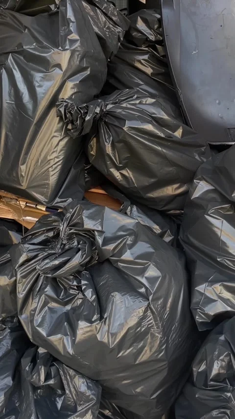 Close-up stack of tied black trash bags on cobblestone curb, glossy wrinkles Stock Footage 344881817