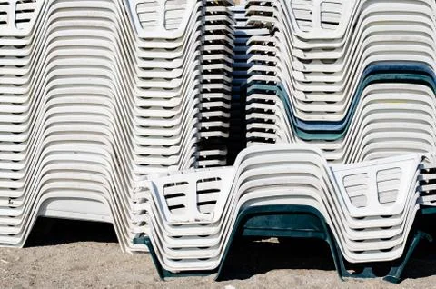 Close-up stack of white and green  plastic  empty chairs on beach . Beginning Stock Photos