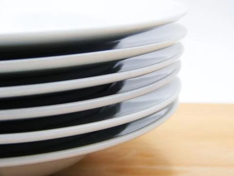 Close-up of stack of white plates on wooden table, white background Stock Photos