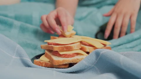 Close up of stacked bread with cheese and meat on bed beside resting hand Stock Footage 318125081