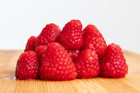 Close up of stacked fresh red raspberry fruits on wooden chopping board. Stock Photos
