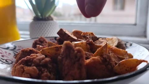 Close-up static shot of a hand picking up a seasoned crispy potato wedge from a Vídeos de archivo 334700055