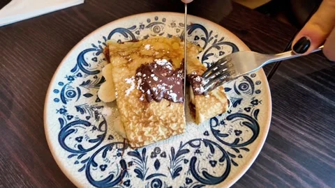 Close-up static shot of a person cutting a chocolate and banana crepe on an orna Stockbeeldmateriaal 332676027